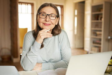 Portrait of gray haired mature businesswoman in eyewear using portable computer for remote work,...