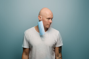 Protective mask hanging on the ear of a bald guy