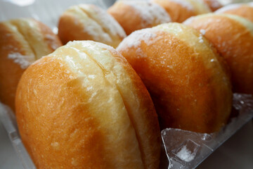 seven round juicy doughnuts sprinkled with powdered sugar lie sideways in a plastic container next to the side view
