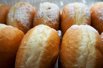 eight round juicy doughnuts sprinkled with powdered sugar lie sideways in plastic packaging close