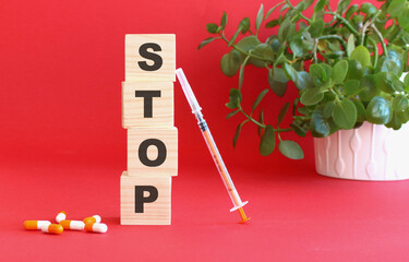 The words STOP is made of wooden cubes on a red background with medical drugs. Medical concept.