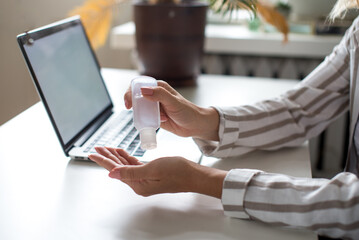 Obraz premium Coronavirus. Sanitizer gel. Business woman working at home, use hand sanitizer aganist covid-19. Quarantine. Cleaning hands antibacterial gel. Stay home. Girl learns, using mockup laptop. Freelance. 