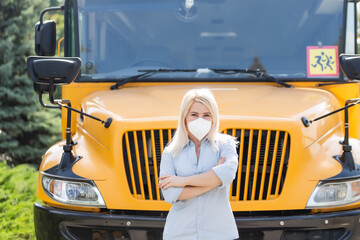 Portrait of beautiful female masked teacher near school bus