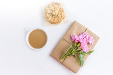 Romantic vintage still life with pretty gift box wrapped with brown craft paper and decorated with pink flower on white background. Dessert (oat cookies) served for tea or coffee break.