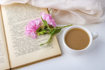 Romantic vintage still life with pink flowers, old book, cup of tea or coffee in spring, summer day in garden. Coffee time