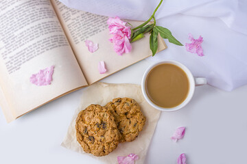 Romantic vintage still life with pink flowers, old book, cup of tea or coffee with milk and oat cookies.