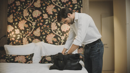 Sexy businessman putting travel bag on bed. Successful man unpacking luggage