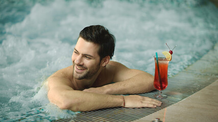 Portrait of sexy guy relaxing in pool at spa hotel. Happy man posing in jacuzzi - obrazy, fototapety, plakaty