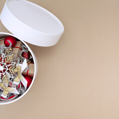 White round box with Christmas decorations in red, white, gold and silver on a beige background.