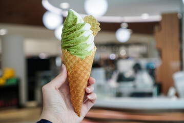 Matcha two tone soft serve ice cream. Woman hand holding a crispy cone of ice cream soft serve with...