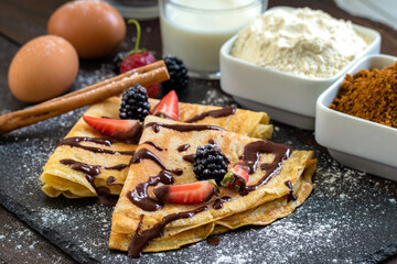 Homemade thin pancakes with ingredients in background.