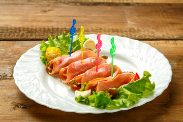 Ham rolls on a plate with cherry salad on a wooden table. save a place.