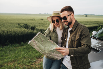 Man and Woman Young Travelers Using Map Near Their Car on Road Trip