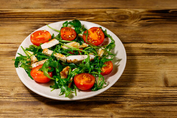Tasty salad of fried chicken breast, fresh arugula and cherry tomatoes on wooden table