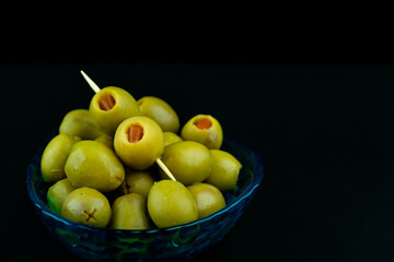 Green olive with red chilli pepper preserved in the little blue bowl on black background