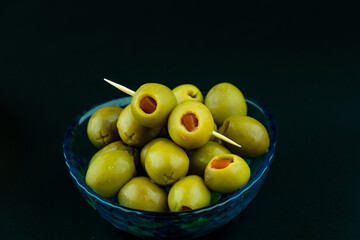 Green olive with red chilli pepper preserved in the little blue bowl on black background