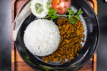 Thai Stir-fried pork with yellow curry paste on white rice served on black dish.