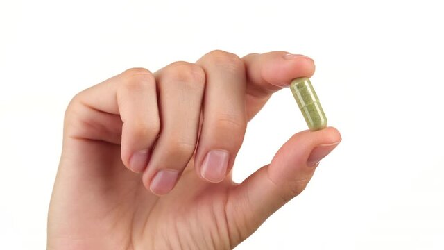 female hand holds in fingers capsule superfoods moringa or spirulina 
