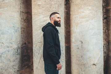 Obraz premium City portrait of handsome hipster guy with beard wearing black blank hoodie or sweatshirt with space for your logo or design. Mockup for print