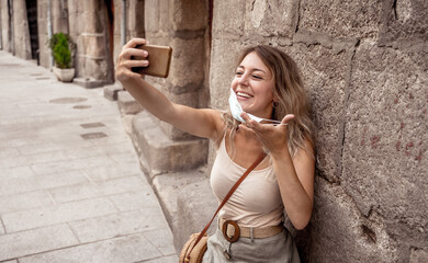 Woman wearing protective face mask with mobile phone video calling friends outdoors city street