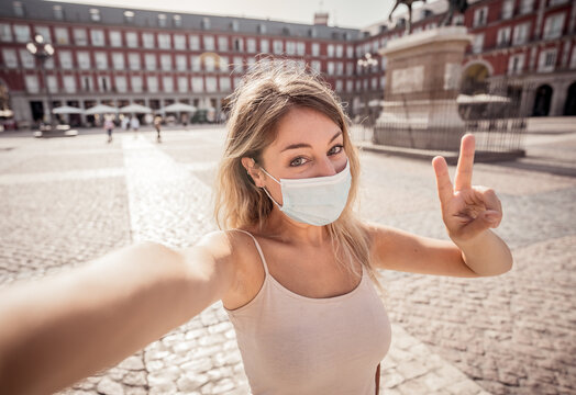 Attractive happy young tourist woman with protective face mask taking a selfie in european city