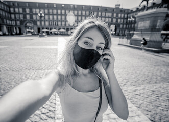 Attractive happy young tourist woman with protective face mask taking a selfie in european city