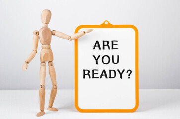 Wooden man shows with a hand to white board with text Are you ready
