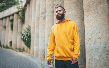 Fototapeta na wymiar City portrait of handsome hipster guy with beard wearing yellow blank hoodie or sweatshirt with space for your logo or design. Mockup for print