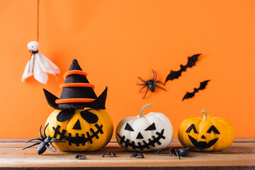 Funny Halloween day decoration party, Cute pumpkin ghost scary jack o lantern face, black spider and bats on wooden table, studio shot isolated on an orange background, Happy holiday concept