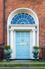 Fototapeta na wymiar Georgian front door, painted blue, with decorative window arch fanlight, stone columns and plant pots. Dublin, Ireland. Iron foot boot scraper, railings and brass hardware