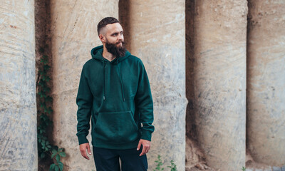 Obraz premium City portrait of handsome hipster guy with beard wearing green (watercolor) blank hoodie or sweatshirt with space for your logo or design. Mockup for print