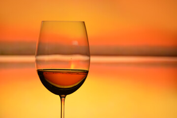 Glass with red wine or fruit drink on the background of the lake at sunset.