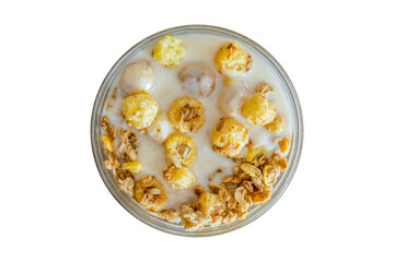 Crunches and corn flakes with yogurt in a transparent glass bowl for cooking in the morning at home on a wooden table in the sunlight, top view.