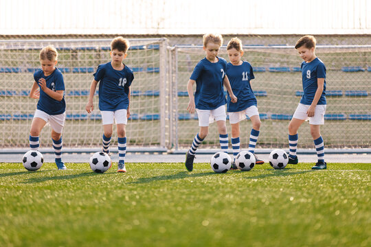 Group of School Boys Kicking Soccer Balls on Grass Sports Pitch. Children Sports Team on School Football Training. Happy Kids Making Sports