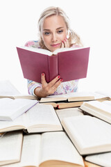 A young girl is reading. A smiling blonde with ponytails on her head sits at a table with books. Knowledge and education. Back to school. Vertical. White background.