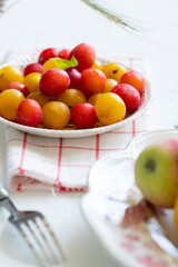 Ripe red and yellow plums and apples on a vintage plate. On light background. Scandinavian style.