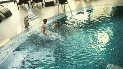 Young couple enjoying hydrotherapy in pool. Happy couple bathing at luxury spa