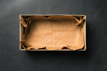 Open empty Shoe box, isolated on a black background. Crumpled brown paper. Packaging for men's and women's shoes or delivery of goods from the store. A top view of a flat layout