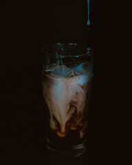 milk pouring into cup of ice cold coffee.