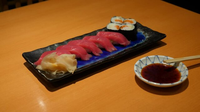 Delicious Japanese food served at regular restaurant, tuna nigirizushi at plate. Man take one piece by chopsticks and dip in soy sauce. Traditional sushi meal, popular in Tokyo