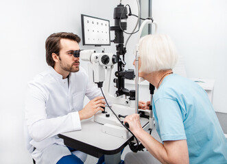 Fototapeta na wymiar Practicing ophthalmologist examines a senior woman patient’s with special ophthalmic equipment in a modern clinic. Vision correction of elderly people