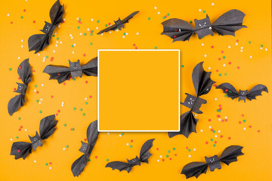 Many bats made of paper on an orange background with decorative multicolored stars. Square area for text in the center. Flat lay. Copy space. The concept of Halloween, and holiday decorations