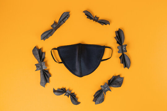 Reusable black anti-virus mask surrounded by paper bats. Orange background. Flat lay. Copy space. The concept of protection from the virus during Halloween