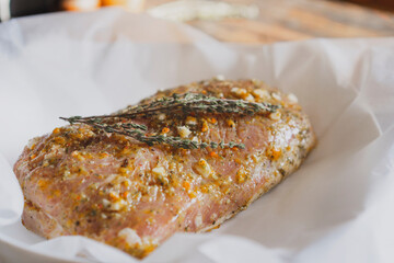 Fresh pork raw carbonade, meat marinated and prepared for roast with garlic, herbs, thyme, spices, pepper on wooden chopping board, rustic table at kitchen. Selective focus, copy space.