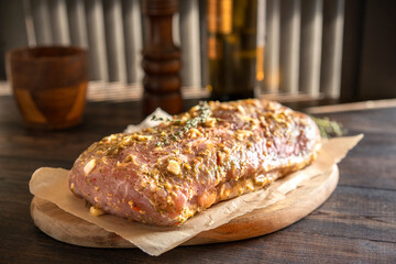 Fresh pork raw carbonade, meat marinated and prepared for roast with garlic, herbs, thyme, spices, pepper on wooden chopping board, rustic table at kitchen. Selective focus, copy space.