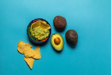Avocado cut in half with guacamole and nachos over a blue surface