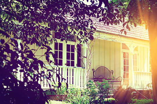 Looking through the opening in the trees at a old traditional villa with an iron bench on veranda. Concept of quite happiness and good old days. Vintage photo - toned image