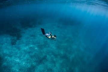 Woman freediver glides over sandy bottom with fins. Freediving in blue sea