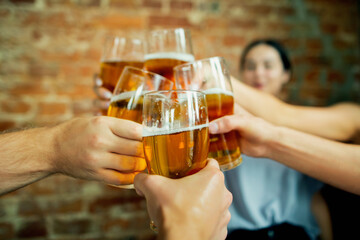Close up clinking. Young group of friends drinking beer, having fun, laughting and celebrating together. Women and men with beer's glasses. Oktoberfest, friendship, togetherness, happiness concept.