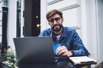 Content young hipster male with laptop and clipboard in cafe